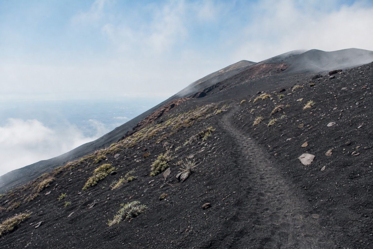 Hikers on a black volcanic sand trail while hiking Mount Etna's slopes